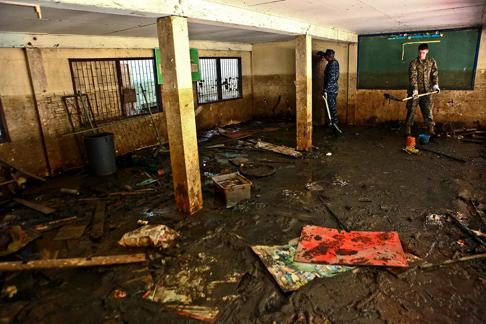 The interior of a building right after a flood, with the floor covered in mud and debris, and staff cleaning up with brooms and shovels