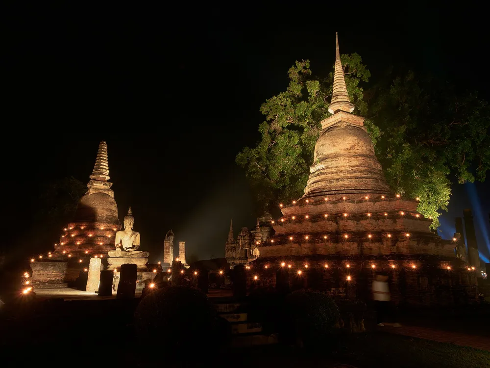 โบราณสถานสุโขทัยยามค่ำคืนที่ประดับด้วยแสงเทียนเรียงรายรอบเจดีย์