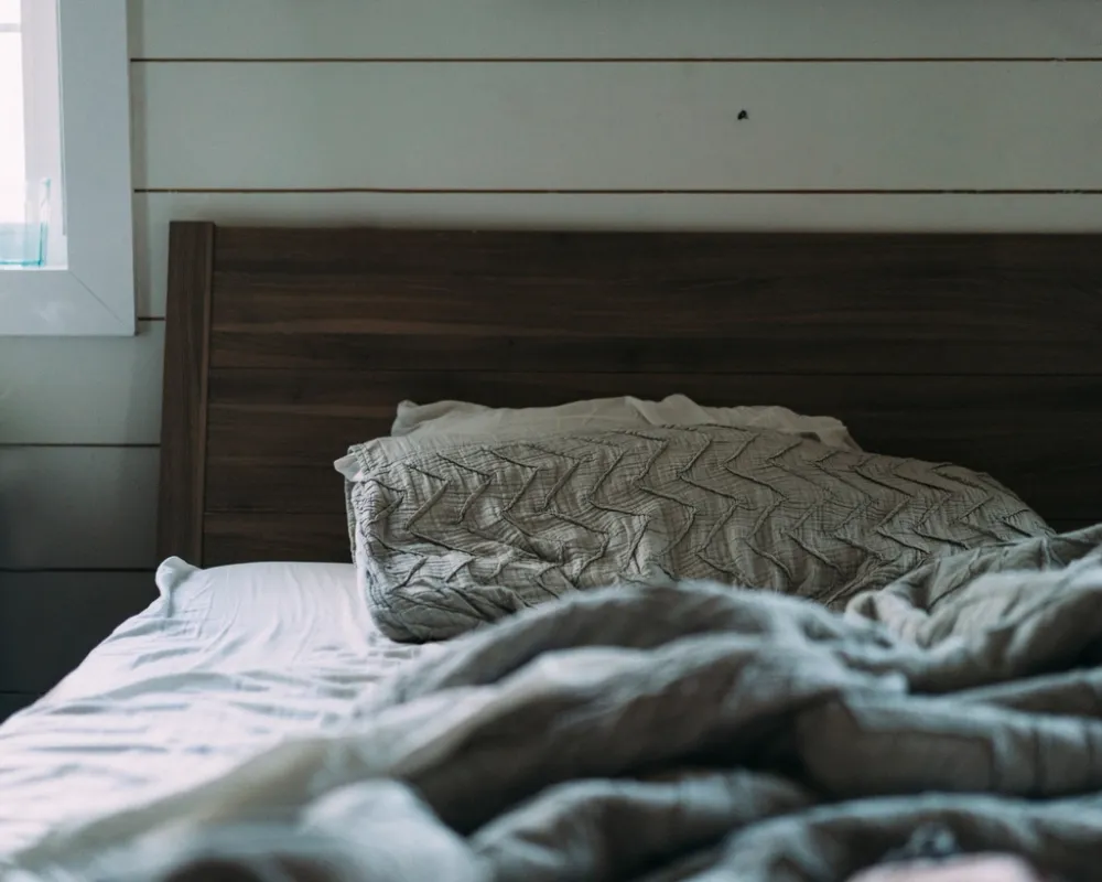 A bed with pillows and a duvet in a bedroom by the window