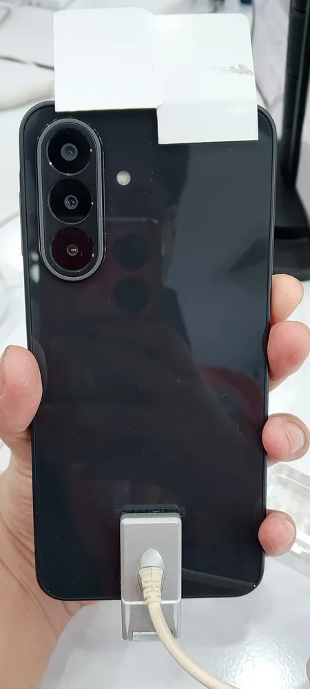 The black Samsung Galaxy A27 5G held in hand, back panel, showing the glossy plastic body and triple-lens camera module