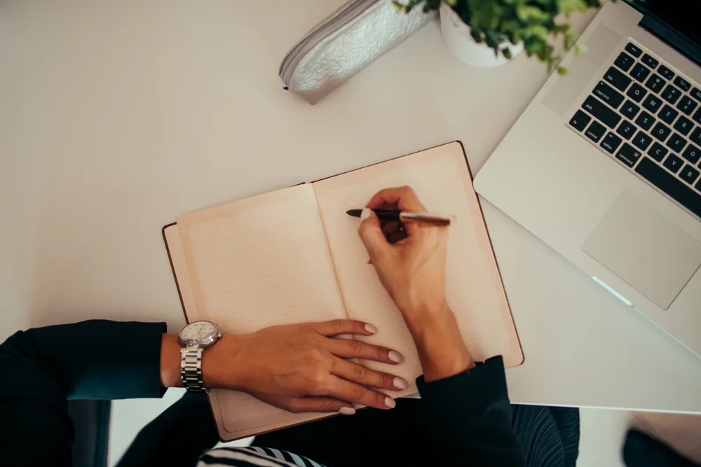 Student writing notes alongside a laptop — study session